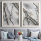 Set of two white barnwood framed canvas prints depicting dramatic organic ink patterns resembling stone veins in soft gray black and champagne tones above a sofa in a contemporary living room.