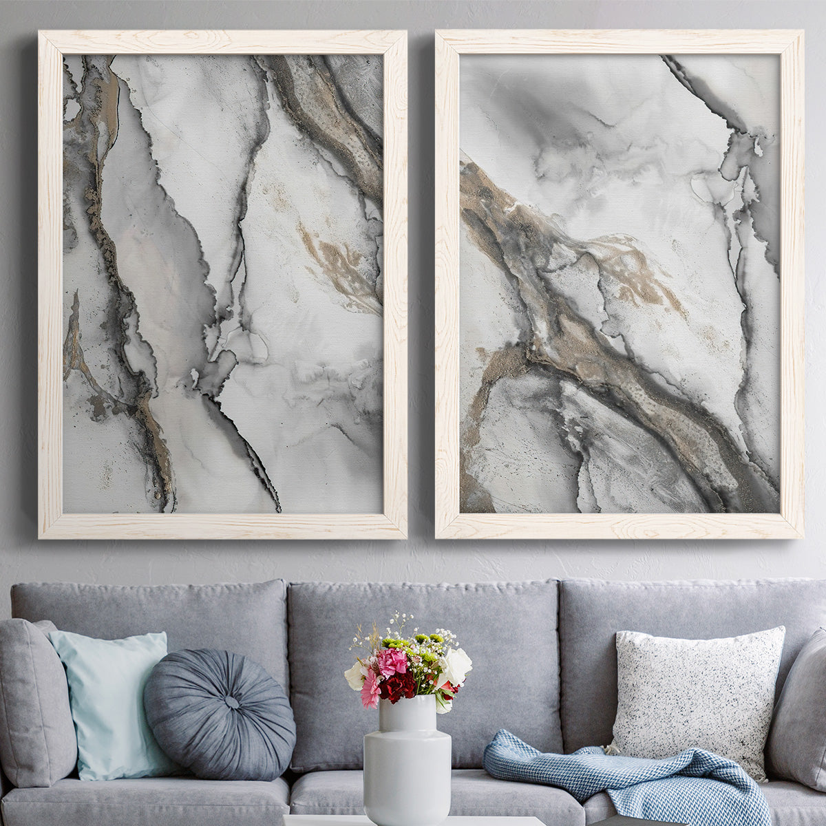 Set of two white barnwood framed canvas prints depicting dramatic organic ink patterns resembling stone veins in soft gray black and champagne tones above a sofa in a contemporary living room.