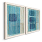 Angled view of a set of two white barnwood framed canvas prints featuring two graphic geometric abstracts featuring stacked blue ovals behind fine vertical stripes.
