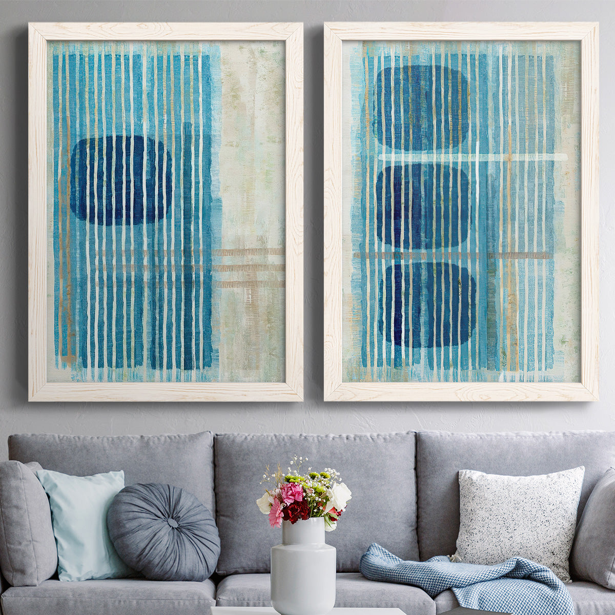 Set of two white barnwood framed canvas prints depicting paired graphic geometric abstracts with navy shapes, turquoise lines, weathered texture, and pale grids above a sofa in a contemporary living room.