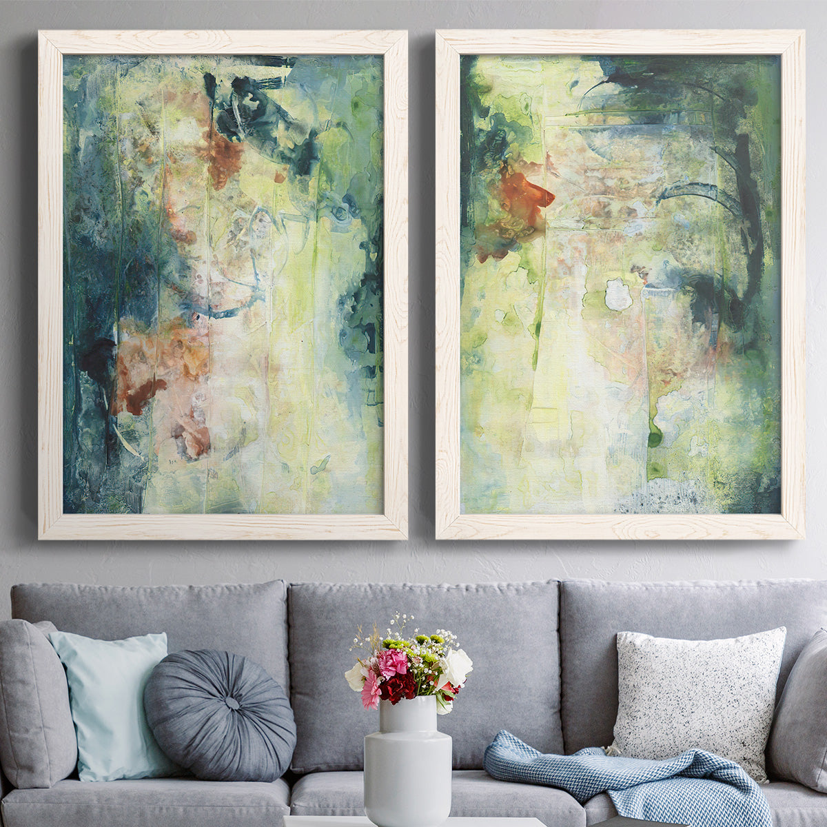 Set of two white barnwood framed canvas prints depicting paired nature-inspired mixed-media abstracts with vertical organic marks, pale light passages, and weathered surfaces above a sofa in a contemporary living room.