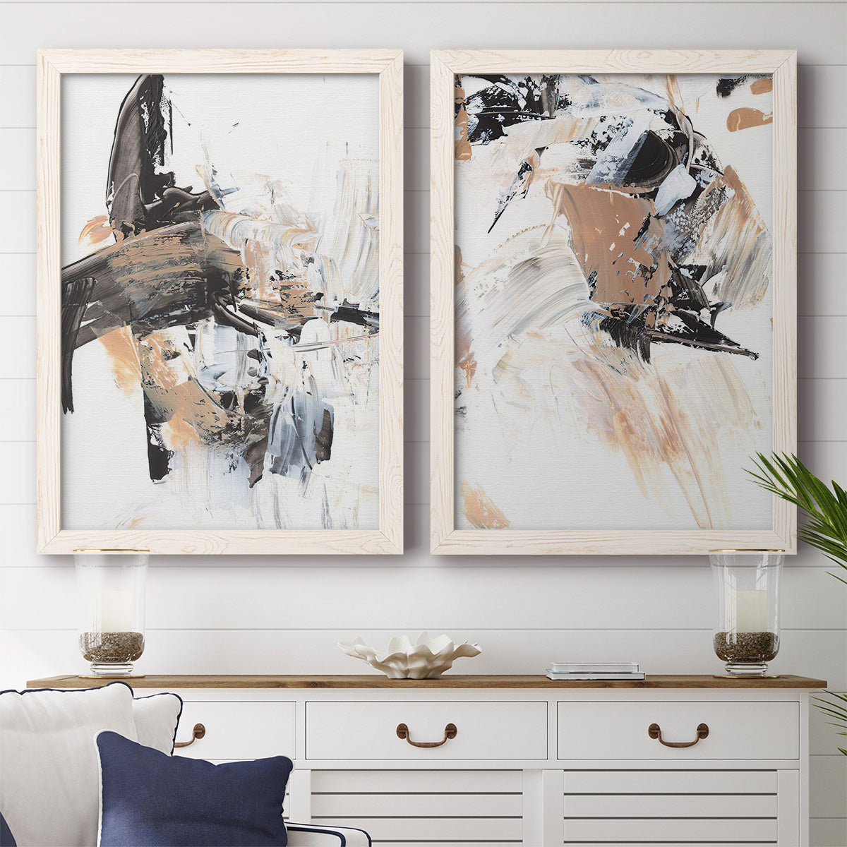 Set of two white barnwood framed canvas prints depicting a coordinated art pair of energetic black white tan and gray painted gestures rendered as bold mixed-media abstracts above a dining room sideboard.