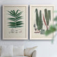 Set of two white barnwood framed canvas prints depicting varied green fronds, roots, spores, and archival labels arranged across two complementary compositions above a sofa in a bright living space.