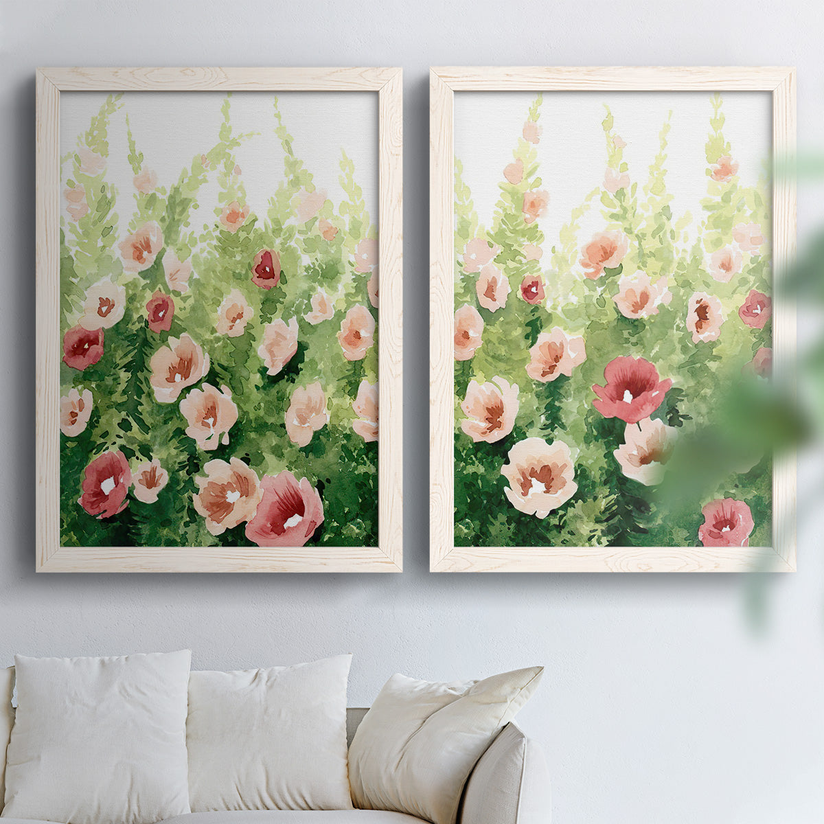 Set of two white barnwood framed canvas prints depicting loose blossoms, green stems, and sunlit watercolor texture arranged across two complementary compositions above a sofa in a bright living space.