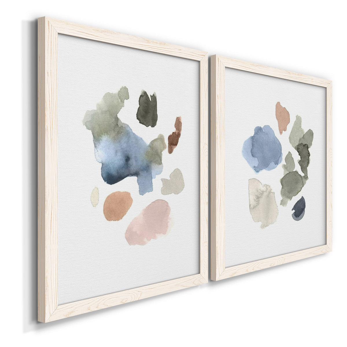 Angled view of a set of two white barnwood framed canvas prints featuring two airy minimalist abstracts featuring scattered translucent watercolor shapes.