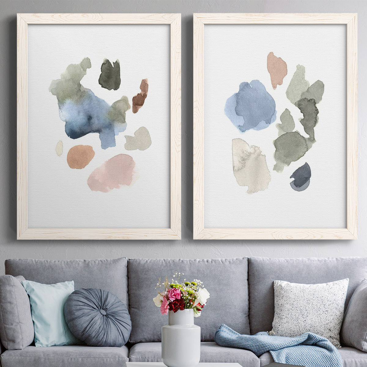 Set of two white barnwood framed canvas prints depicting paired airy minimalist abstracts with muted blue green blush and charcoal forms floating on white above a sofa in a contemporary living room.