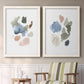 Set of two white barnwood framed canvas prints depicting two airy minimalist abstracts featuring scattered translucent watercolor shapes above a sideboard in a cozy sitting room.