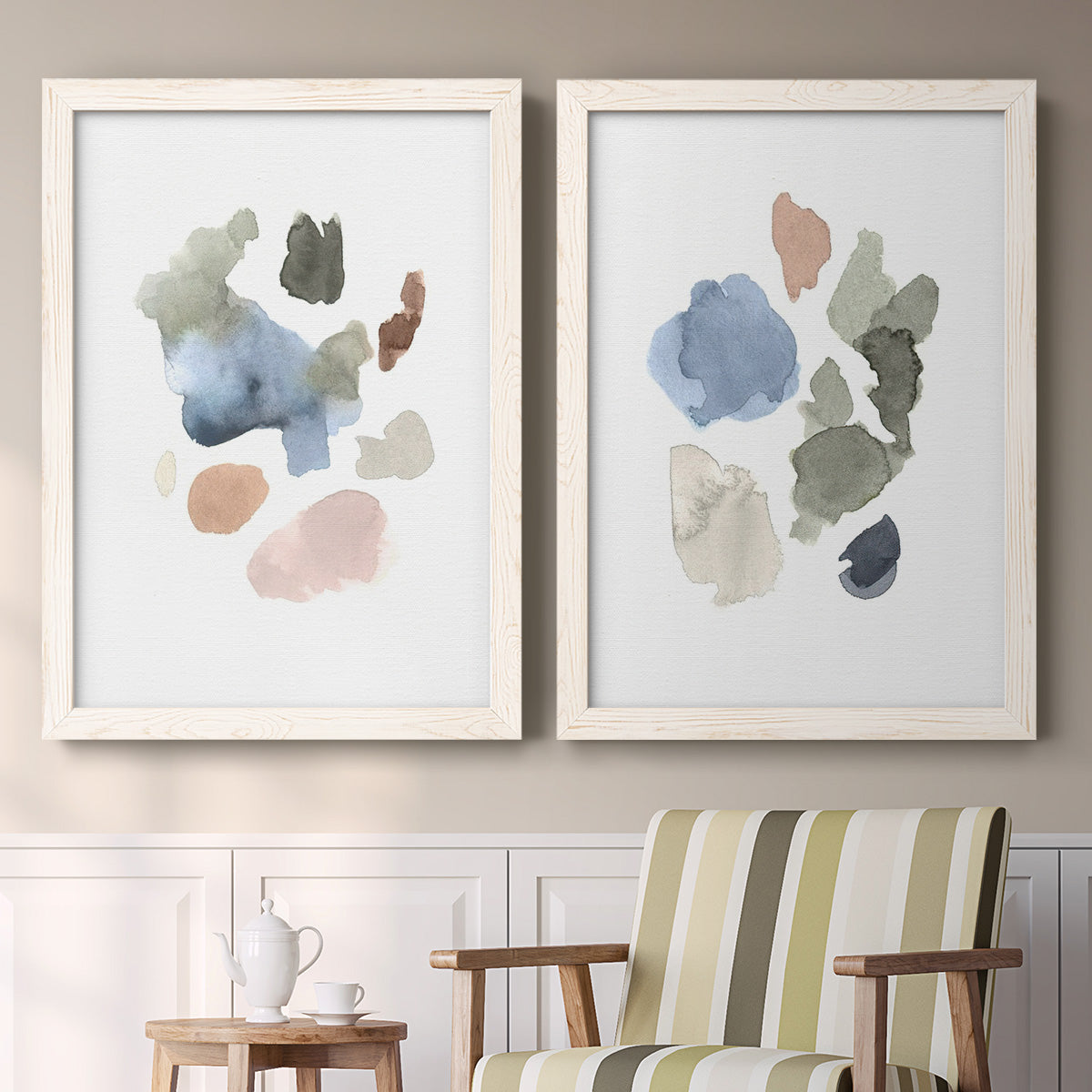 Set of two white barnwood framed canvas prints depicting two airy minimalist abstracts featuring scattered translucent watercolor shapes above a sideboard in a cozy sitting room.