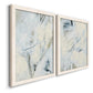 Angled view of a set of two white barnwood framed canvas prints featuring two airy gestural abstracts featuring pale blue cream and charcoal marks drifting across white.