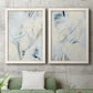 Set of two white barnwood framed canvas prints depicting a coordinated art pair of pale blue cream and charcoal marks drifting across white rendered as airy gestural abstracts above a sofa in a modern living room.