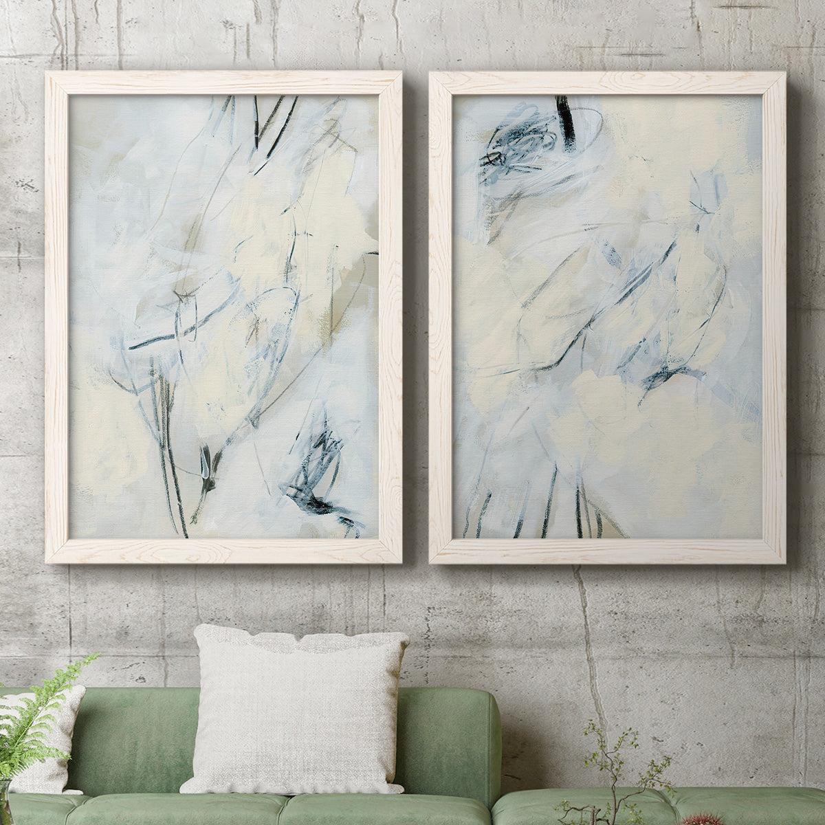 Set of two white barnwood framed canvas prints depicting a coordinated art pair of pale blue cream and charcoal marks drifting across white rendered as airy gestural abstracts above a sofa in a modern living room.