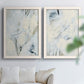 Set of two white barnwood framed canvas prints depicting fine angular lines, faint washes, and scattered dark accents arranged across two complementary compositions above a sofa in a bright living space.