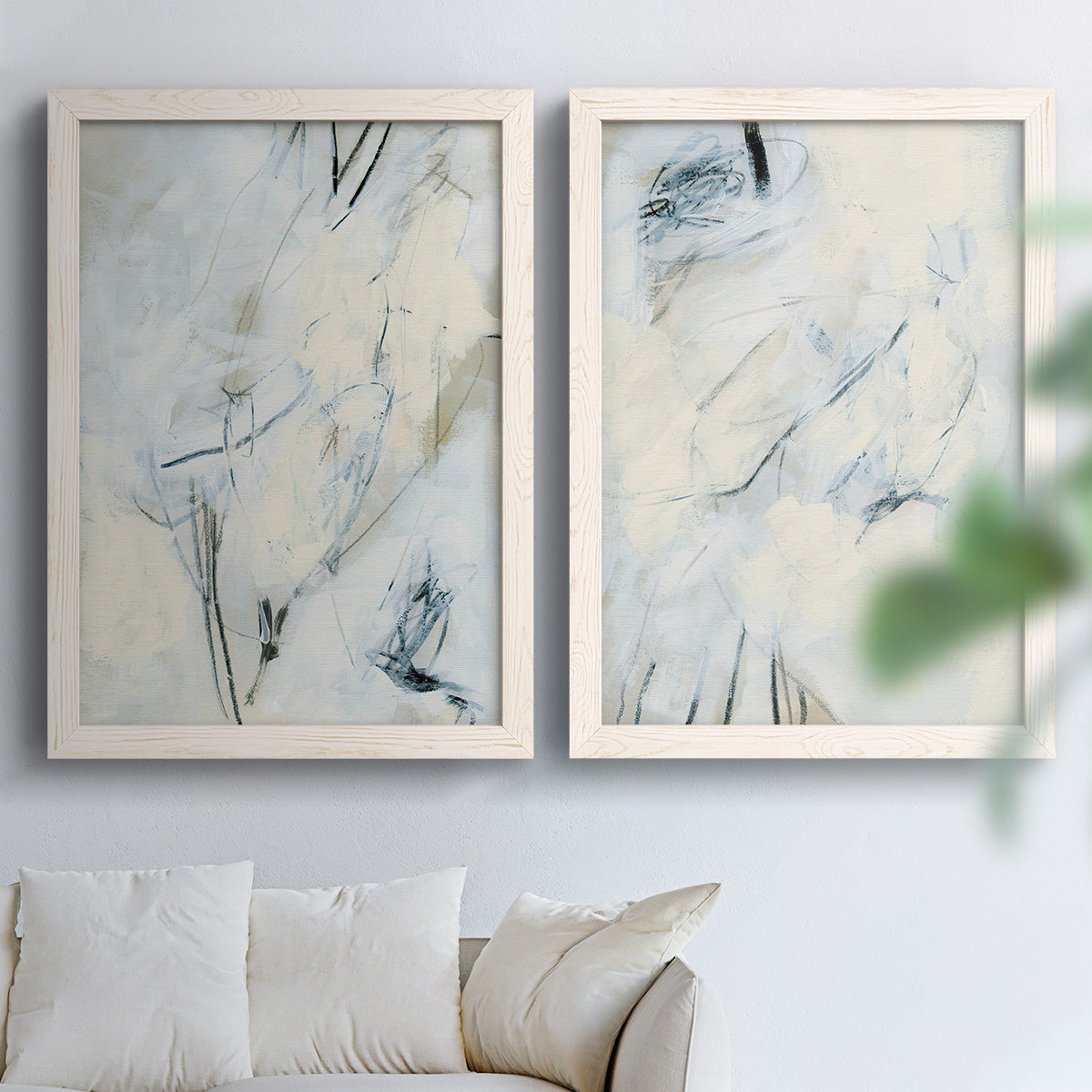 Set of two white barnwood framed canvas prints depicting fine angular lines, faint washes, and scattered dark accents arranged across two complementary compositions above a sofa in a bright living space.