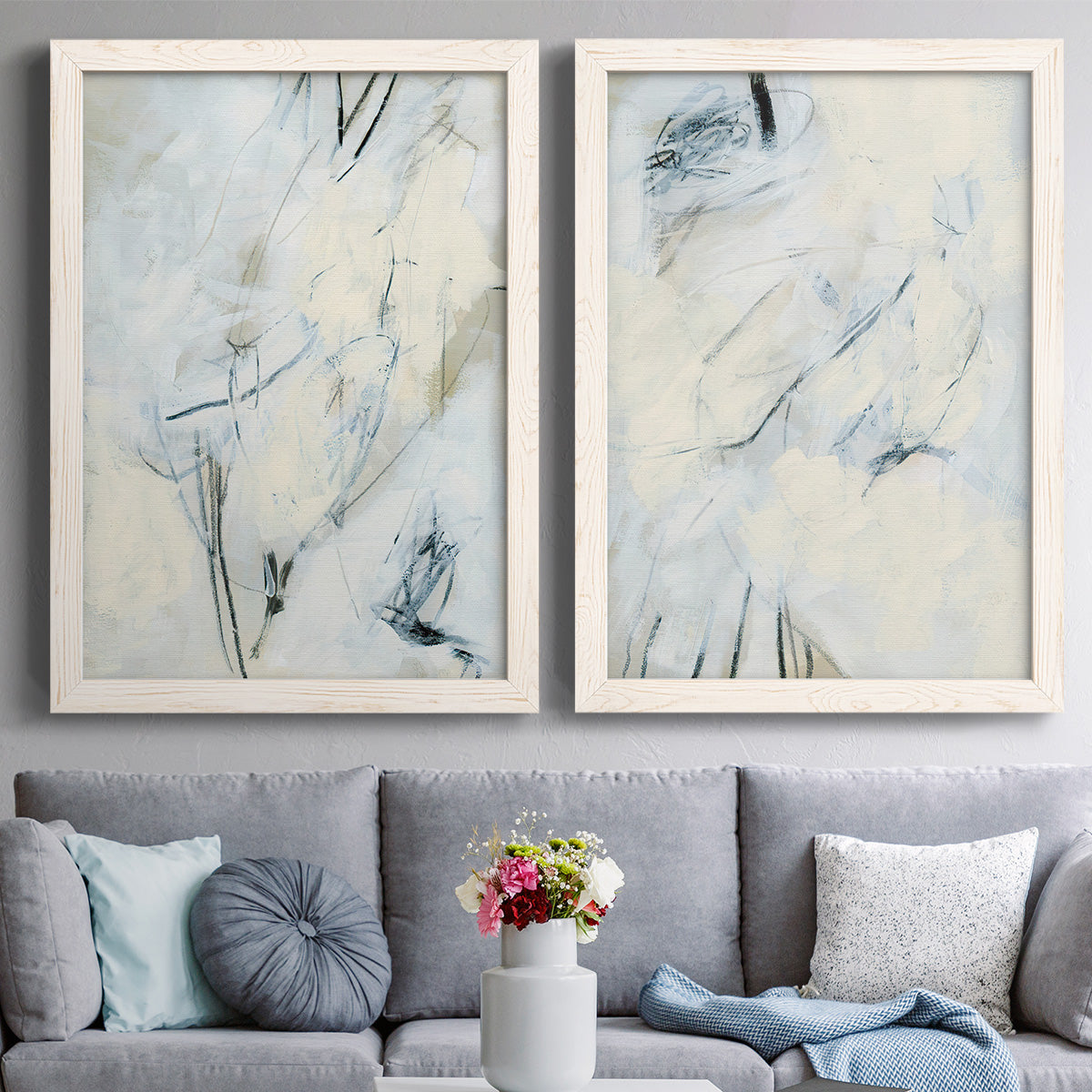 Set of two white barnwood framed canvas prints depicting paired airy gestural abstracts with fine angular lines, faint washes, and scattered dark accents above a sofa in a contemporary living room.