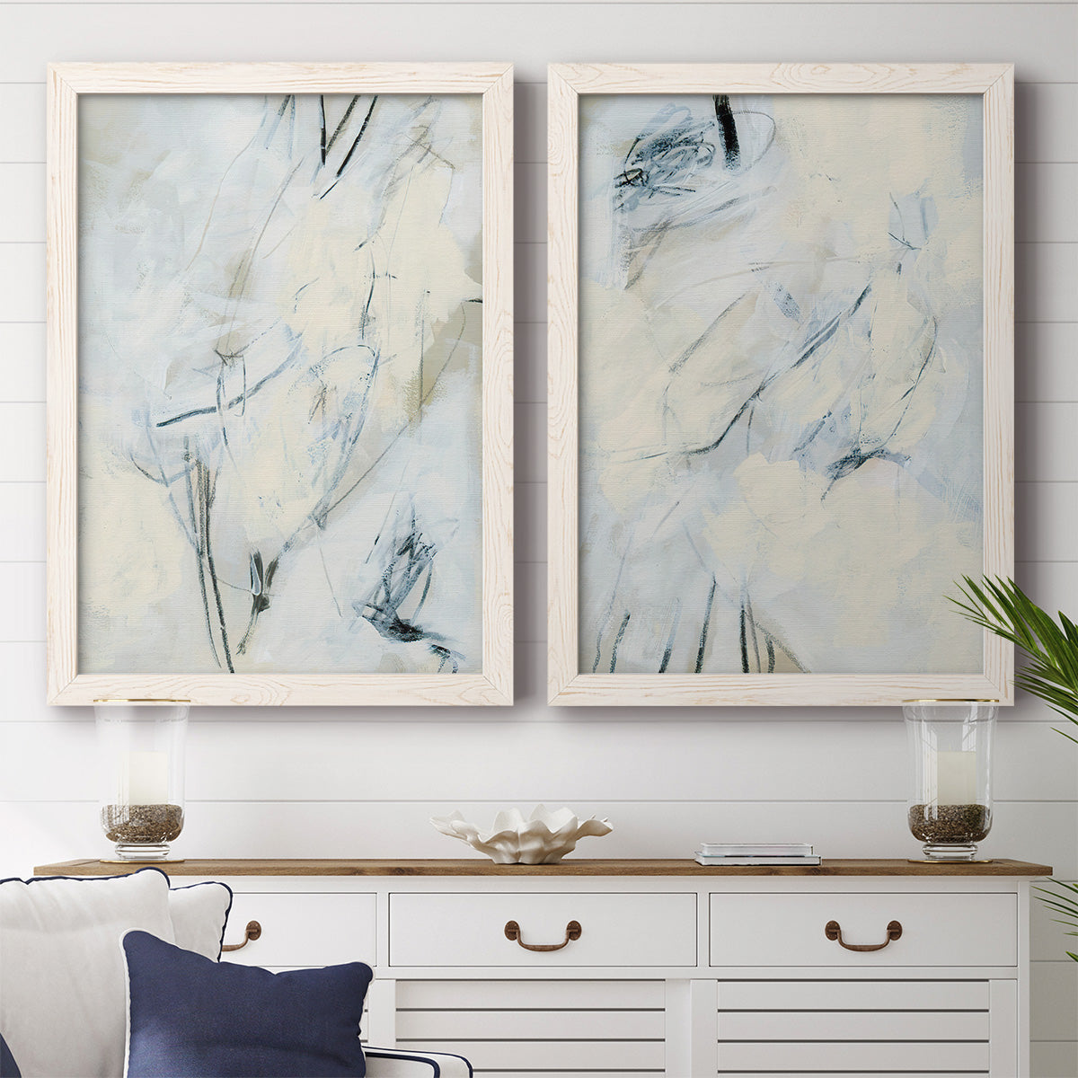 Set of two white barnwood framed canvas prints depicting a coordinated art pair of pale blue cream and charcoal marks drifting across white rendered as airy gestural abstracts above a dining room sideboard.
