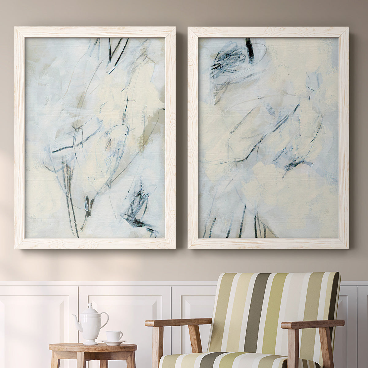 Set of two white barnwood framed canvas prints depicting two airy gestural abstracts featuring pale blue cream and charcoal marks drifting across white above a sideboard in a cozy sitting room.