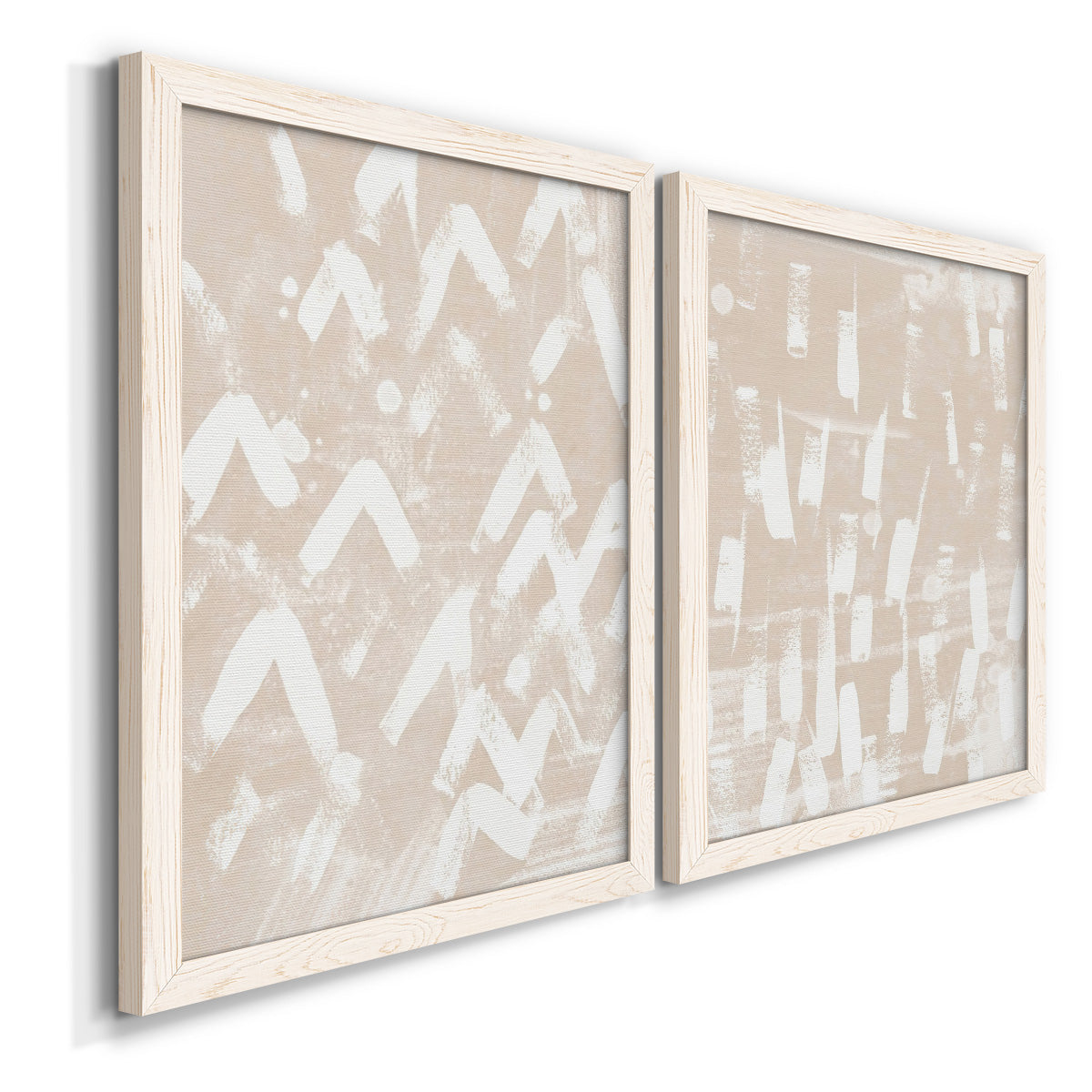 Angled view of a set of two white barnwood framed canvas prints featuring two tribal-inspired pattern abstracts featuring white hand-painted dashes arcs and chevrons.