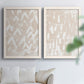Set of two white barnwood framed canvas prints depicting repeating marks, warm beige grounds, and block-print texture arranged across two complementary compositions above a sofa in a bright living space.