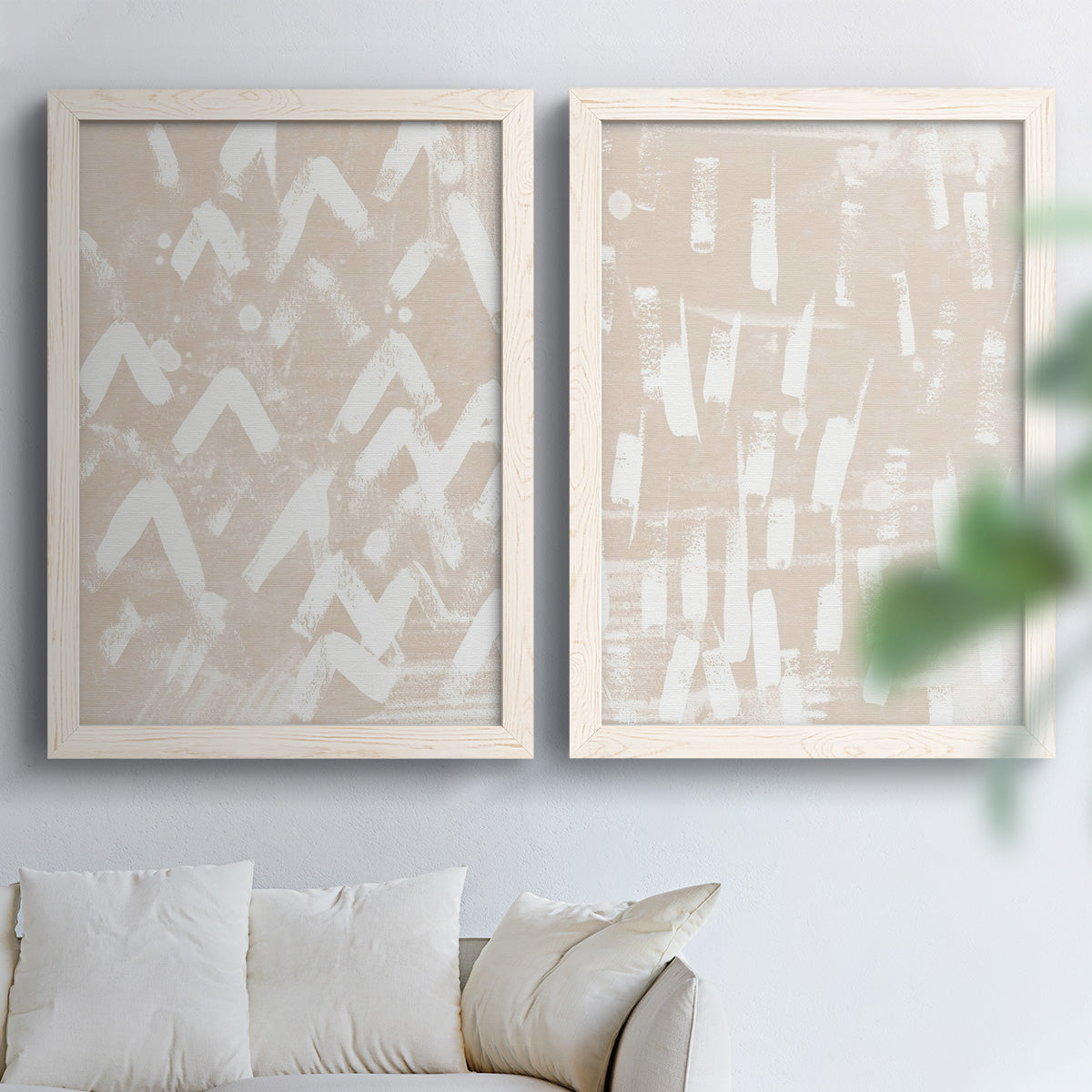 Set of two white barnwood framed canvas prints depicting repeating marks, warm beige grounds, and block-print texture arranged across two complementary compositions above a sofa in a bright living space.