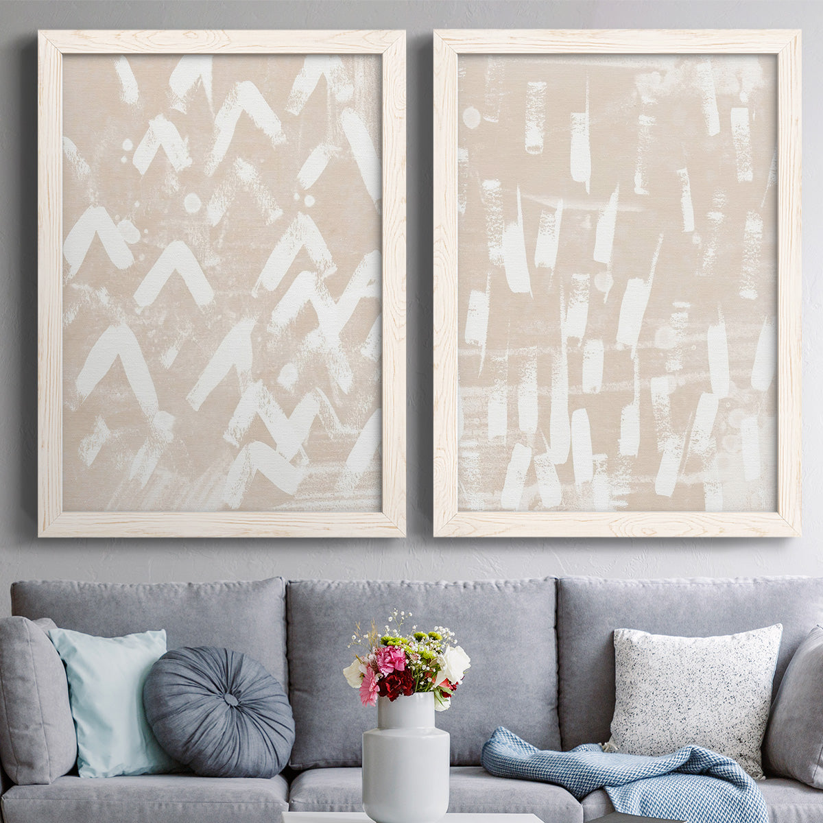 Set of two white barnwood framed canvas prints depicting paired tribal-inspired pattern abstracts with repeating marks, warm beige grounds, and block-print texture above a sofa in a contemporary living room.
