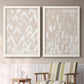 Set of two white barnwood framed canvas prints depicting two tribal-inspired pattern abstracts featuring white hand-painted dashes arcs and chevrons above a sideboard in a cozy sitting room.
