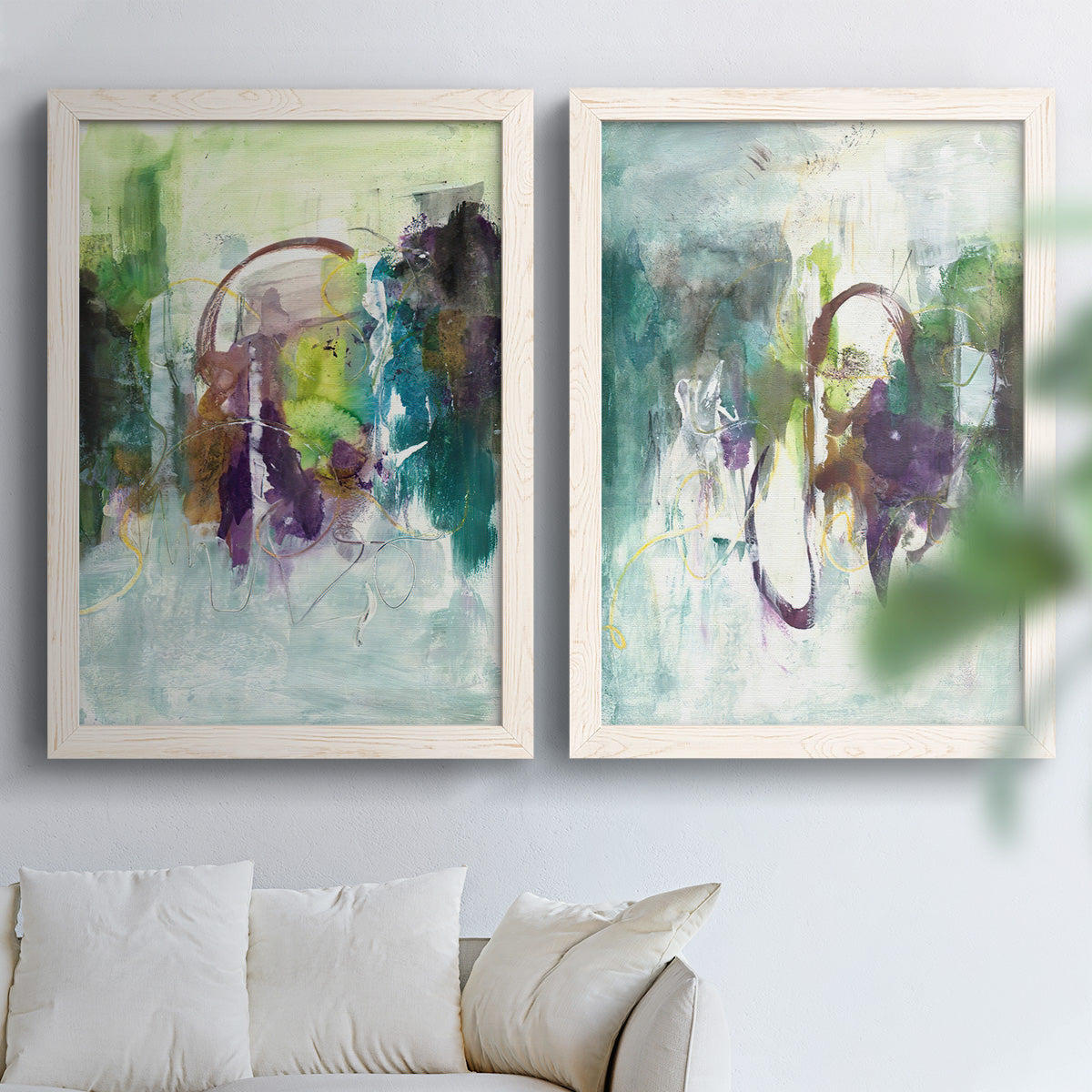 Set of two white barnwood framed canvas prints depicting soft-edged color masses, looping lines, and pale blue grounds arranged across two complementary compositions above a sofa in a bright living space.