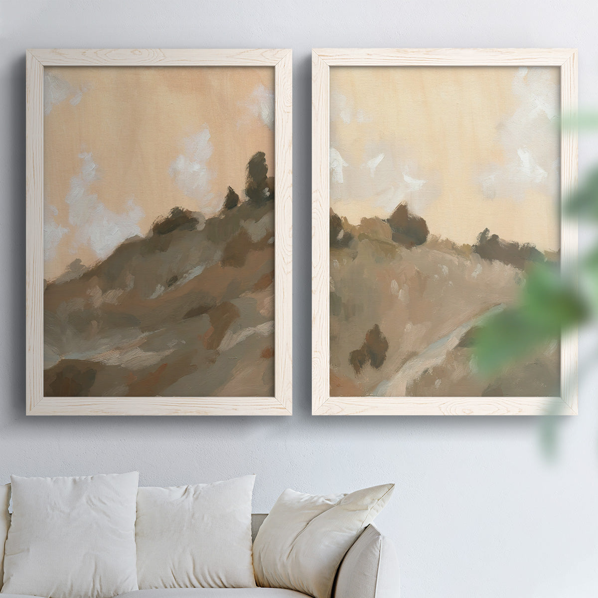 Set of two white barnwood framed canvas prints depicting layered ridges, soft earth tones, and hazy cream skies arranged across two complementary compositions above a sofa in a bright living space.