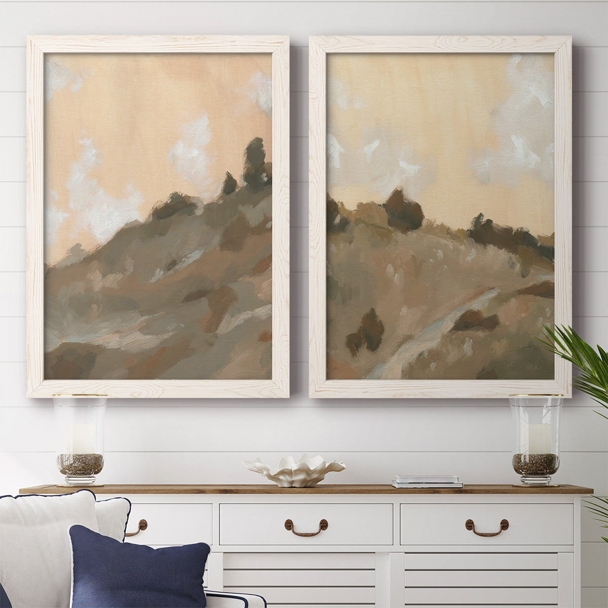 Set of two white barnwood framed canvas prints depicting a coordinated art pair of misty brown hills and winding mountain paths rendered as minimalist watercolor landscapes above a dining room sideboard.
