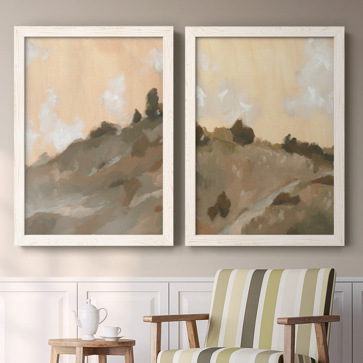 Set of two white barnwood framed canvas prints depicting two minimalist watercolor landscapes featuring misty brown hills and winding mountain paths above a sideboard in a cozy sitting room.