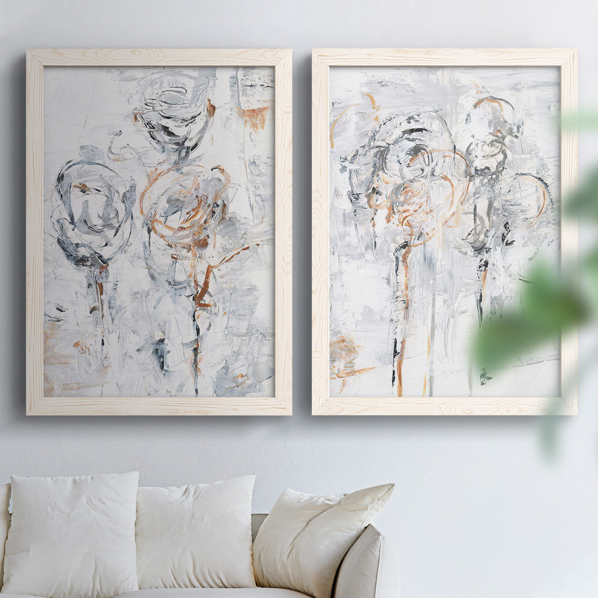 Set of two white barnwood framed canvas prints depicting scribbled outlines, creamy paint, and delicate warm accents arranged across two complementary compositions above a sofa in a bright living space.