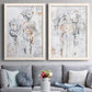 Set of two white barnwood framed canvas prints depicting paired expressive floral abstracts with scribbled outlines, creamy paint, and delicate warm accents above a sofa in a contemporary living room.