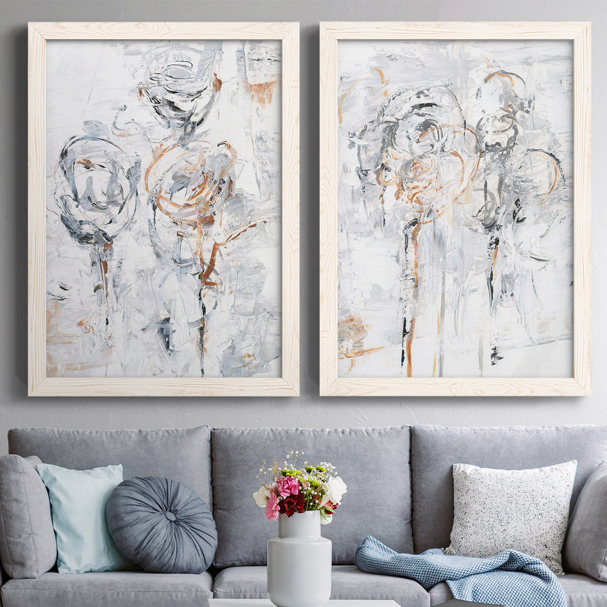 Set of two white barnwood framed canvas prints depicting paired expressive floral abstracts with scribbled outlines, creamy paint, and delicate warm accents above a sofa in a contemporary living room.
