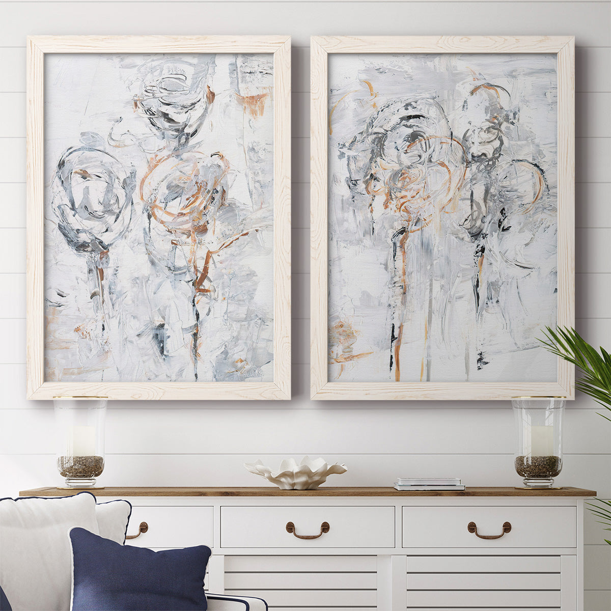Set of two white barnwood framed canvas prints depicting a coordinated art pair of loosely suggested flowers and stems in pale gray and peach rendered as expressive floral abstracts above a dining room sideboard.