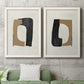 Set of two white barnwood framed canvas prints depicting a coordinated art pair of black brown and cream cutout-like forms rendered as minimalist geometric collage abstracts above a sofa in a modern living room.