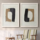 Set of two white barnwood framed canvas prints depicting two minimalist geometric collage abstracts featuring black brown and cream cutout-like forms above a sideboard in a cozy sitting room.