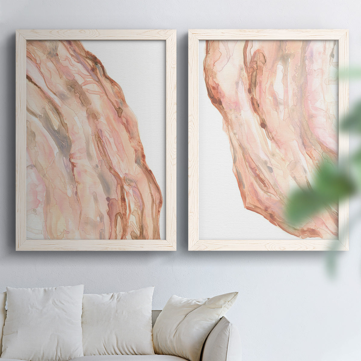 Set of two white barnwood framed canvas prints depicting layered translucent striations, warm pink veins, and luminous white areas arranged across two complementary compositions above a sofa in a bright living space.