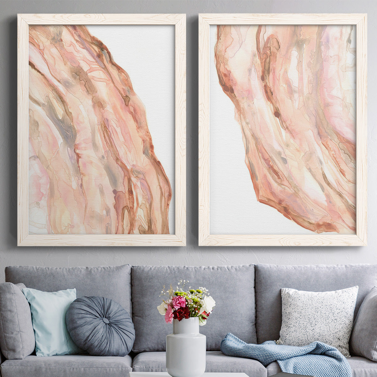 Set of two white barnwood framed canvas prints depicting paired soft marble-inspired abstracts with layered translucent striations, warm pink veins, and luminous white areas above a sofa in a contemporary living room.