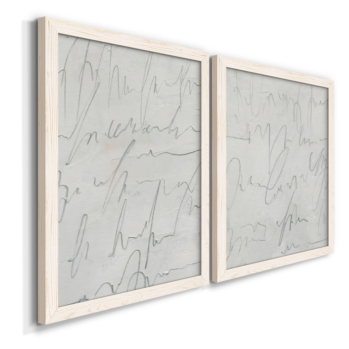 Angled view of a set of two white barnwood framed canvas prints featuring two minimalist script abstracts featuring faint looping handwriting across pale gray grounds.