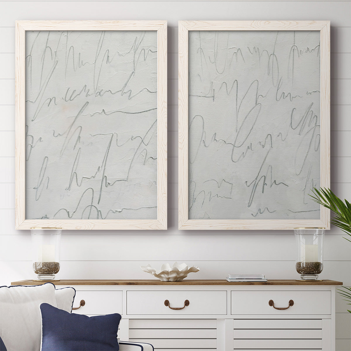 Set of two white barnwood framed canvas prints depicting a coordinated art pair of faint looping handwriting across pale gray grounds rendered as minimalist script abstracts above a dining room sideboard.