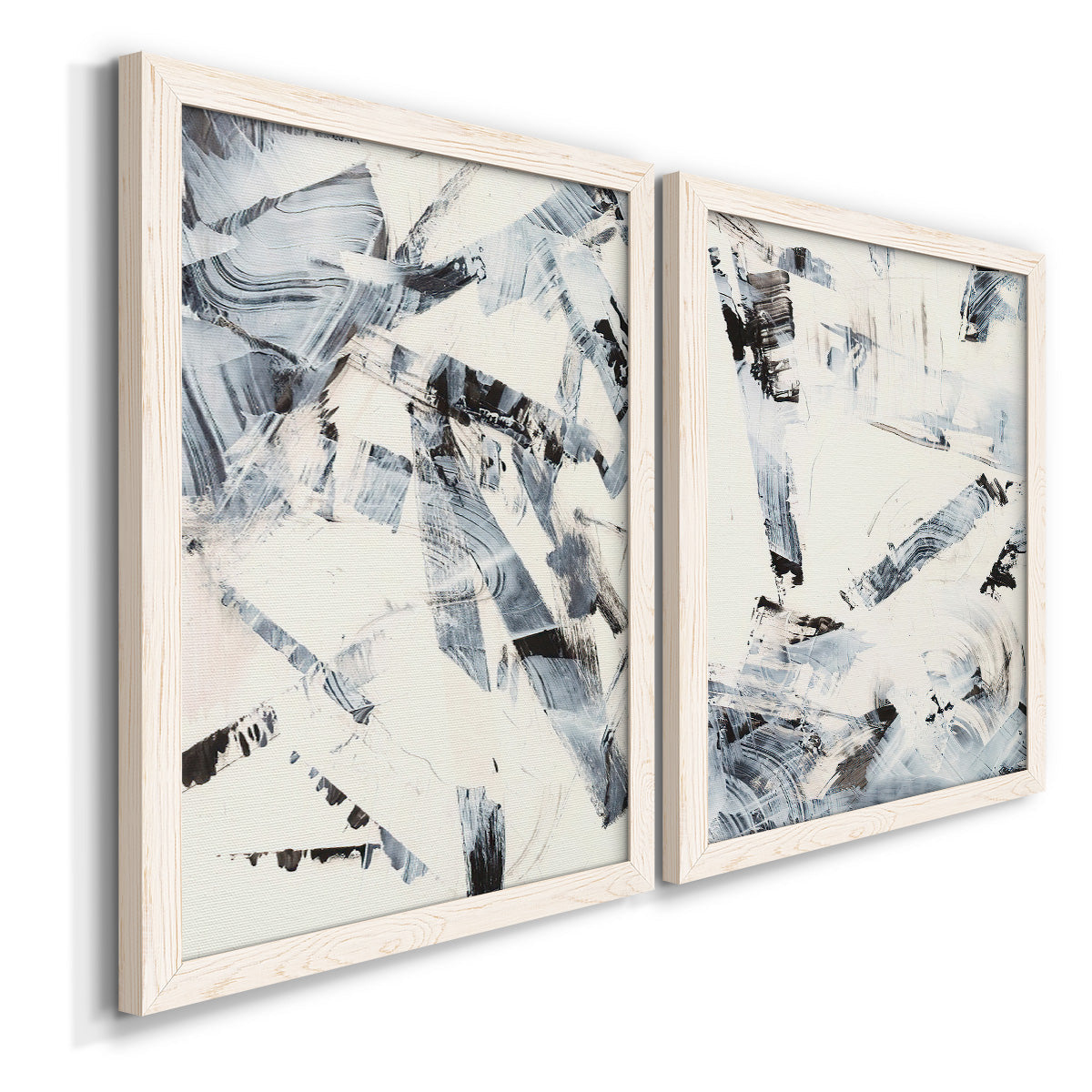 Angled view of a set of two white barnwood framed canvas prints featuring two high-contrast gestural abstracts featuring angular black and gray brush fragments on white.