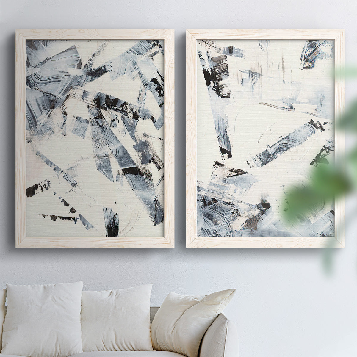 Set of two white barnwood framed canvas prints depicting broken strokes, scraped textures, and intersecting monochrome shapes arranged across two complementary compositions above a sofa in a bright living space.
