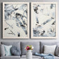 Set of two white barnwood framed canvas prints depicting paired high-contrast gestural abstracts with broken strokes, scraped textures, and intersecting monochrome shapes above a sofa in a contemporary living room.