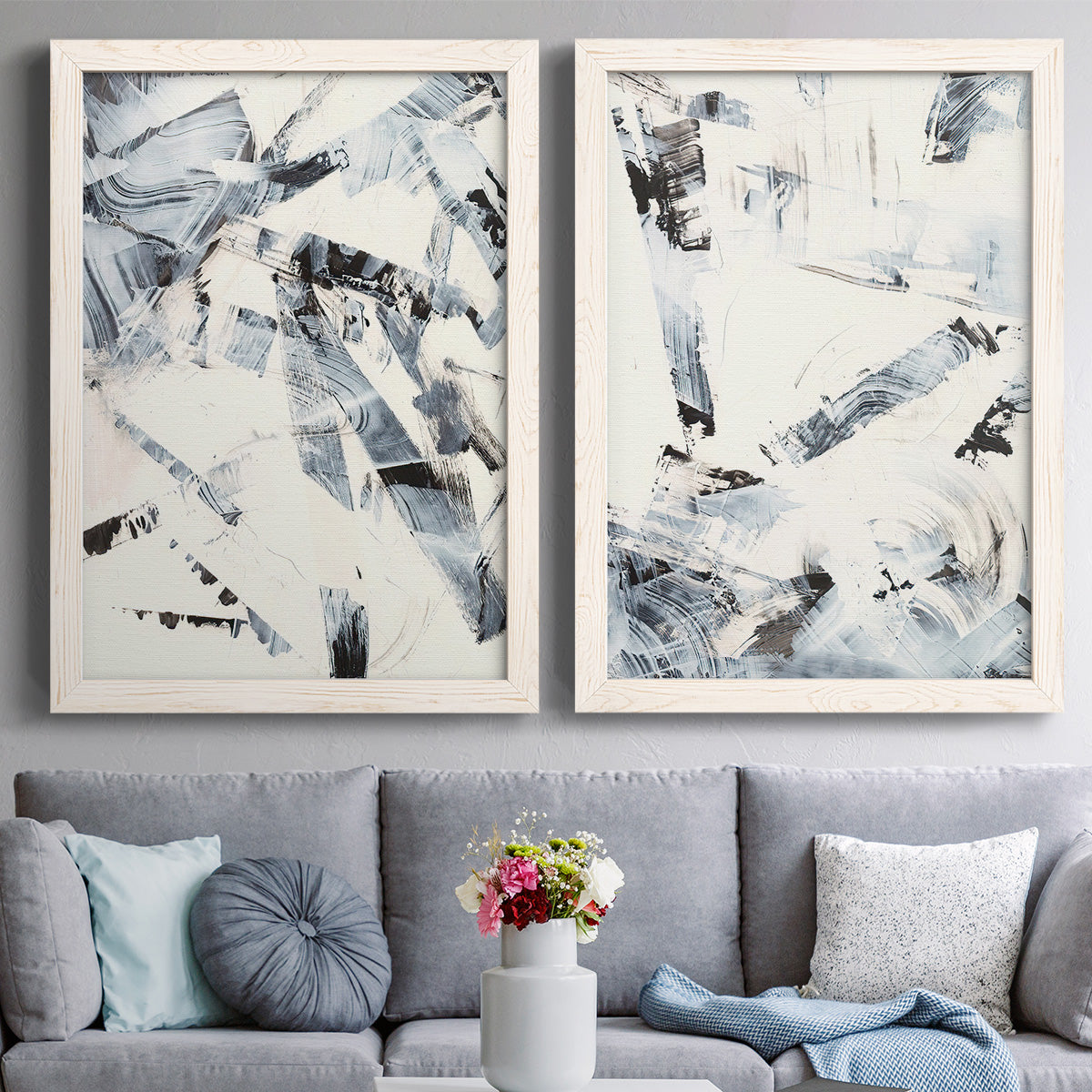 Set of two white barnwood framed canvas prints depicting paired high-contrast gestural abstracts with broken strokes, scraped textures, and intersecting monochrome shapes above a sofa in a contemporary living room.