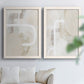 Set of two white barnwood framed canvas prints depicting calm modern compositions with translucent taupe forms pale gray fields and textured cream accents above a sofa in a bright living space.