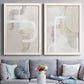 Set of two white barnwood framed canvas prints depicting interlocking organic geometry in warm neutral tones with broad white paths and subtle surface texture above a sofa in a contemporary living room.