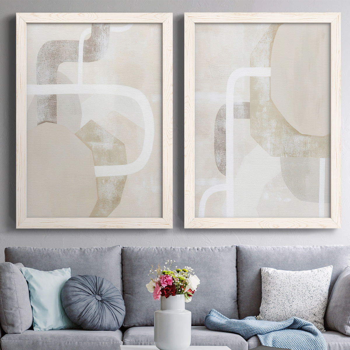 Set of two white barnwood framed canvas prints depicting interlocking organic geometry in warm neutral tones with broad white paths and subtle surface texture above a sofa in a contemporary living room.
