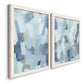 Angled view of a set of two white barnwood framed canvas prints featuring two cool-toned geometric abstracts featuring fragmented pale blue green gray and white brush blocks.