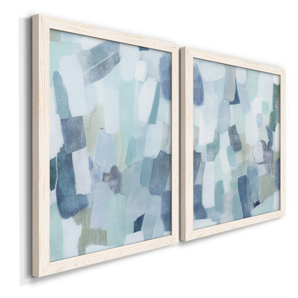 Angled view of a set of two white barnwood framed canvas prints featuring two cool-toned geometric abstracts featuring fragmented pale blue green gray and white brush blocks.