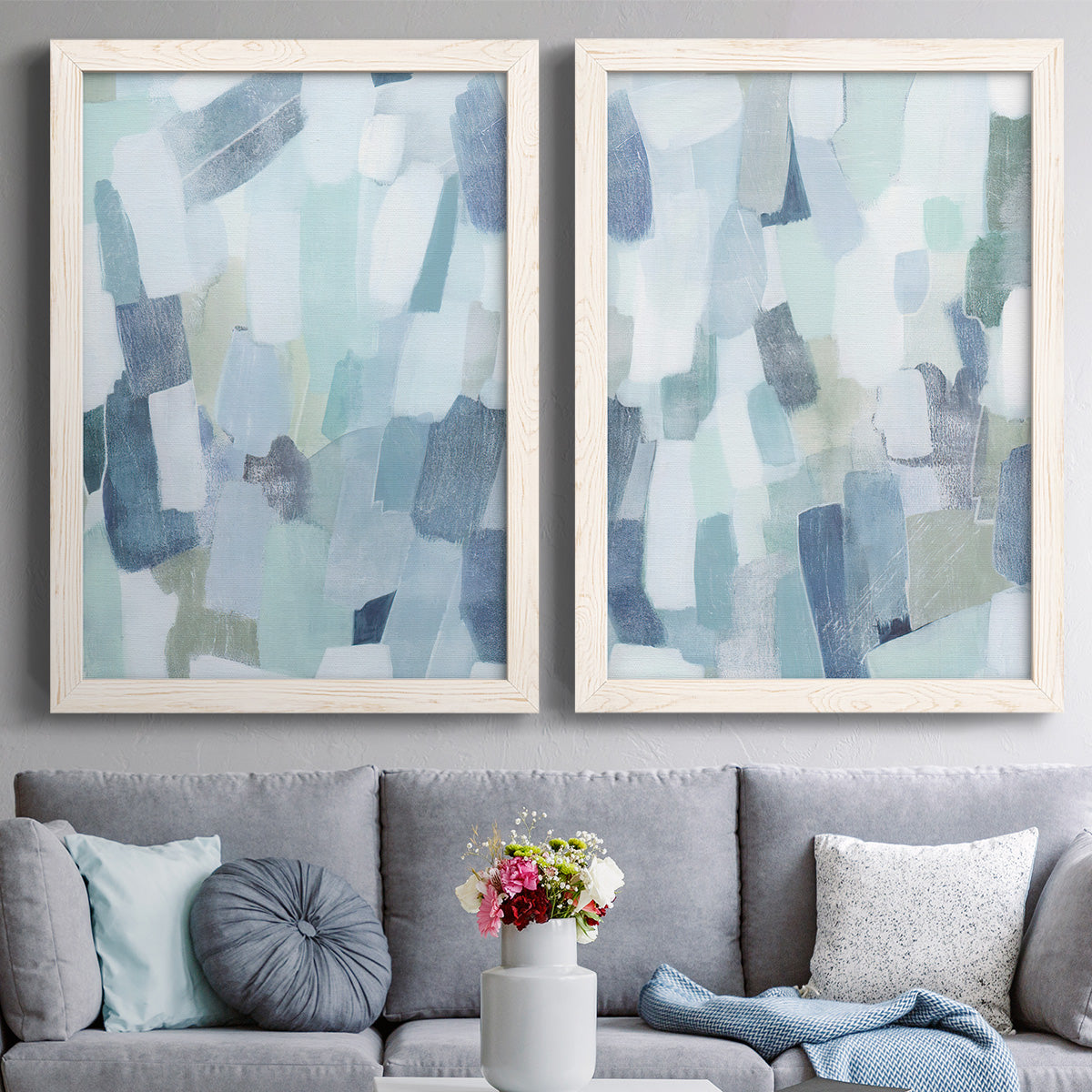 Set of two white barnwood framed canvas prints depicting paired cool-toned geometric abstracts with overlapping rectangular marks and softly weathered paint above a sofa in a contemporary living room.