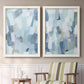 Set of two white barnwood framed canvas prints depicting two cool-toned geometric abstracts featuring fragmented pale blue green gray and white brush blocks above a sideboard in a cozy sitting room.